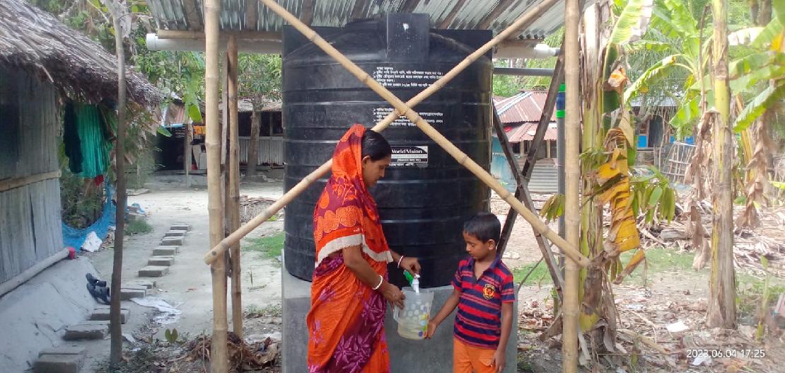 한 여성이 아동에게 식수탱크에서 물을 떠서 주고 있다.